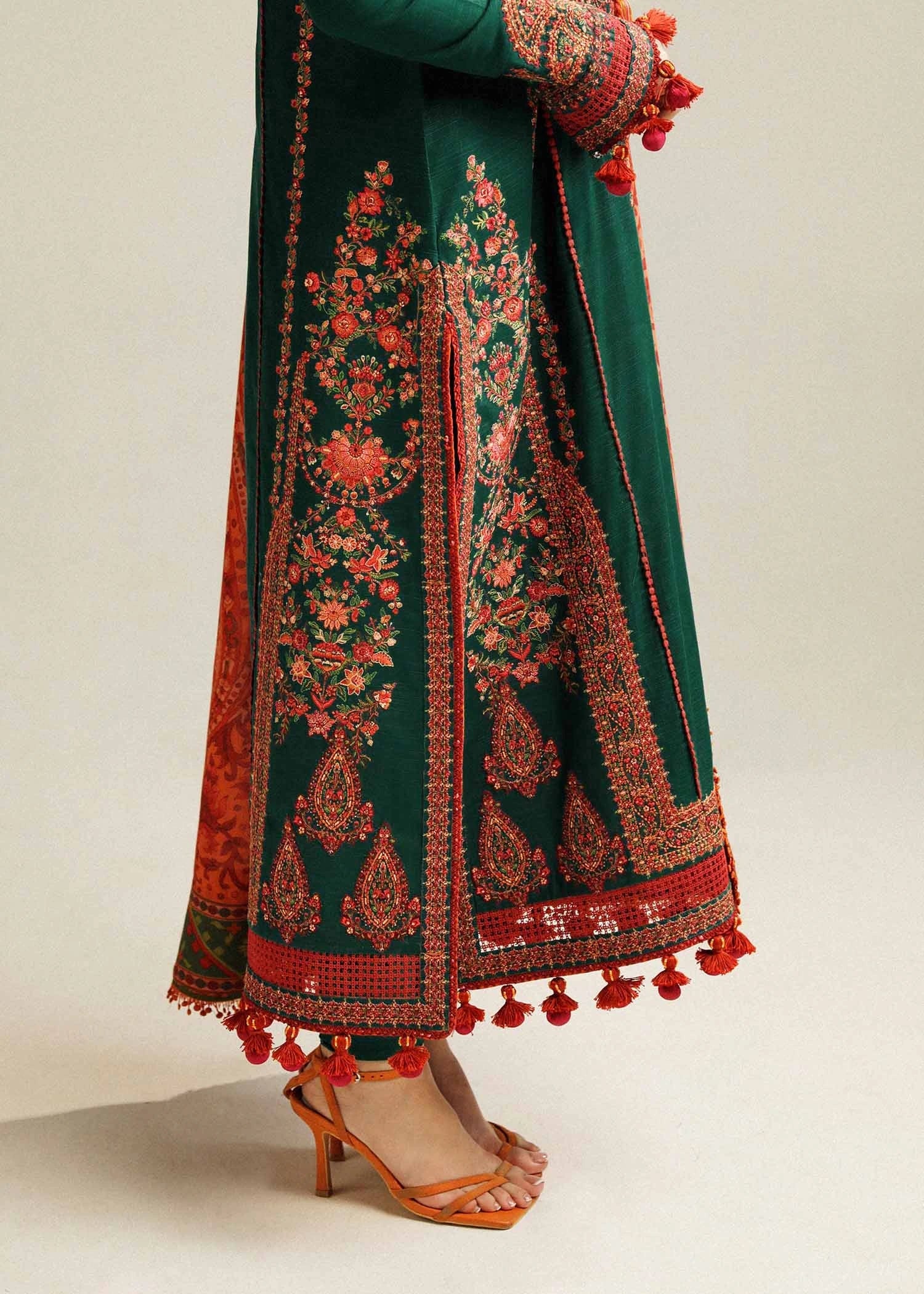 Green and red embroidered traditional outfit with tassels on a neutral background