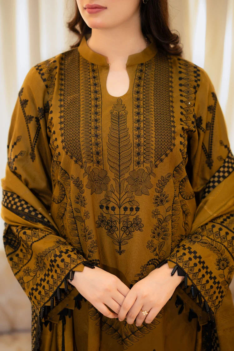Woman wearing a mustard yellow dress with black intricate patterns against a neutral background